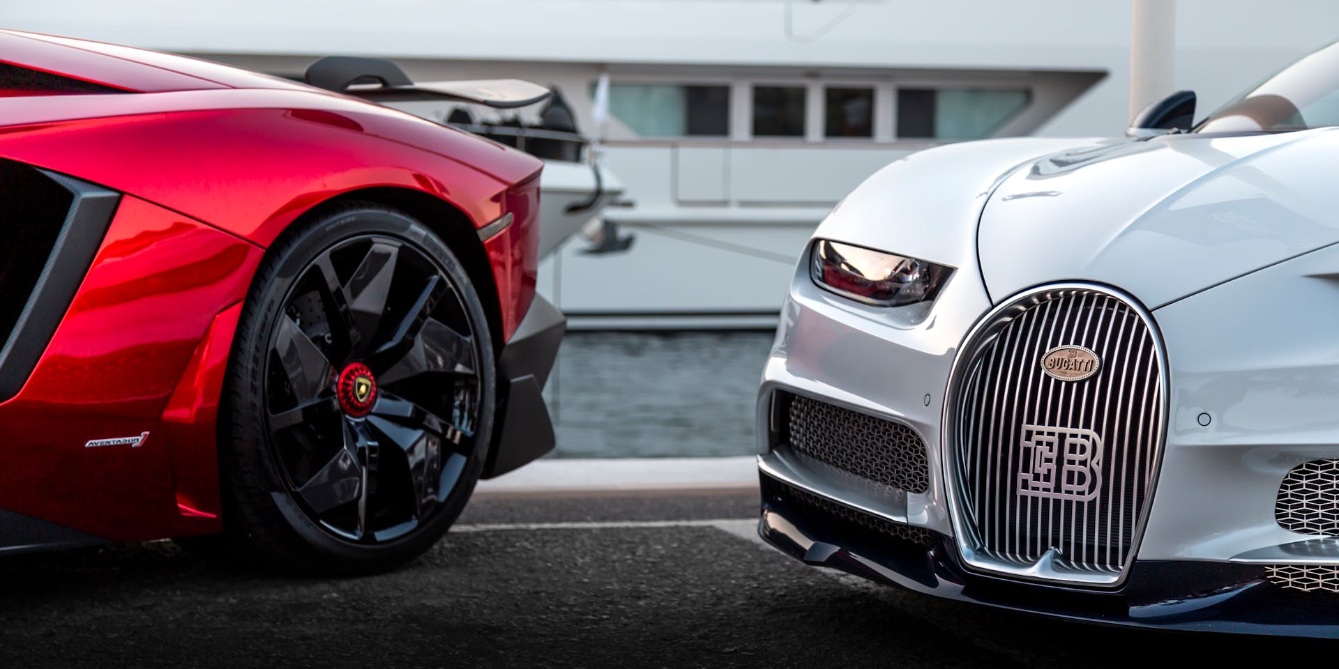 Close-up of two luxury supercars parked by a marina, showcasing elegance and design.