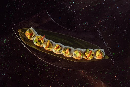 Delicious sushi roll topped with avocado and peppers, beautifully presented on a leaf, perfect for Asian cuisine lovers.