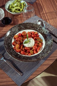 A top view of a vibrant Caprese salad with cherry tomatoes and mozzarella on a wooden table.
