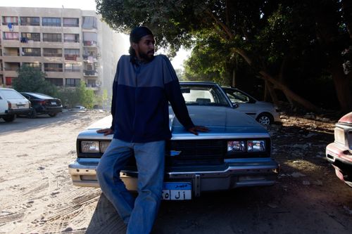 Free A fashionable man poses with a vintage Chevrolet car in an outdoor urban setting. Stock Photo