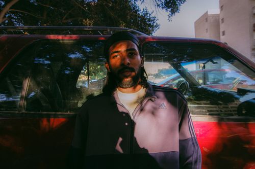 Free Portrait of a fashionable man leaning on a vintage car in urban sunlight. Stock Photo