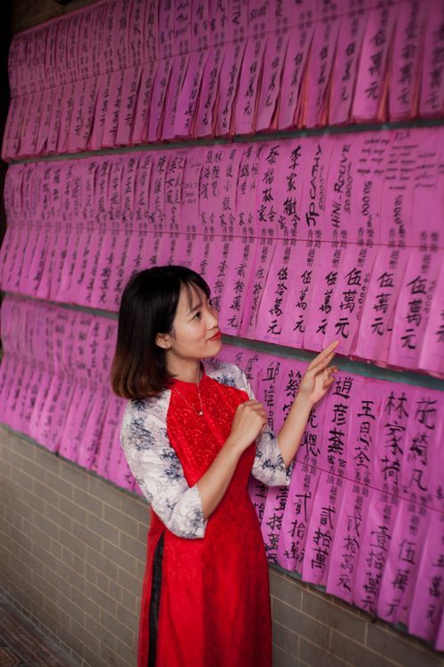 Free A woman in a red dress examines traditional prayer papers hanging on a wall. Stock Photo