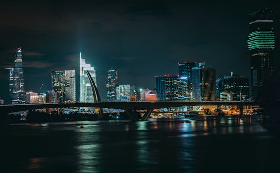 Stunning nighttime cityscape with glowing skyscrapers and a bridge reflecting on the water.