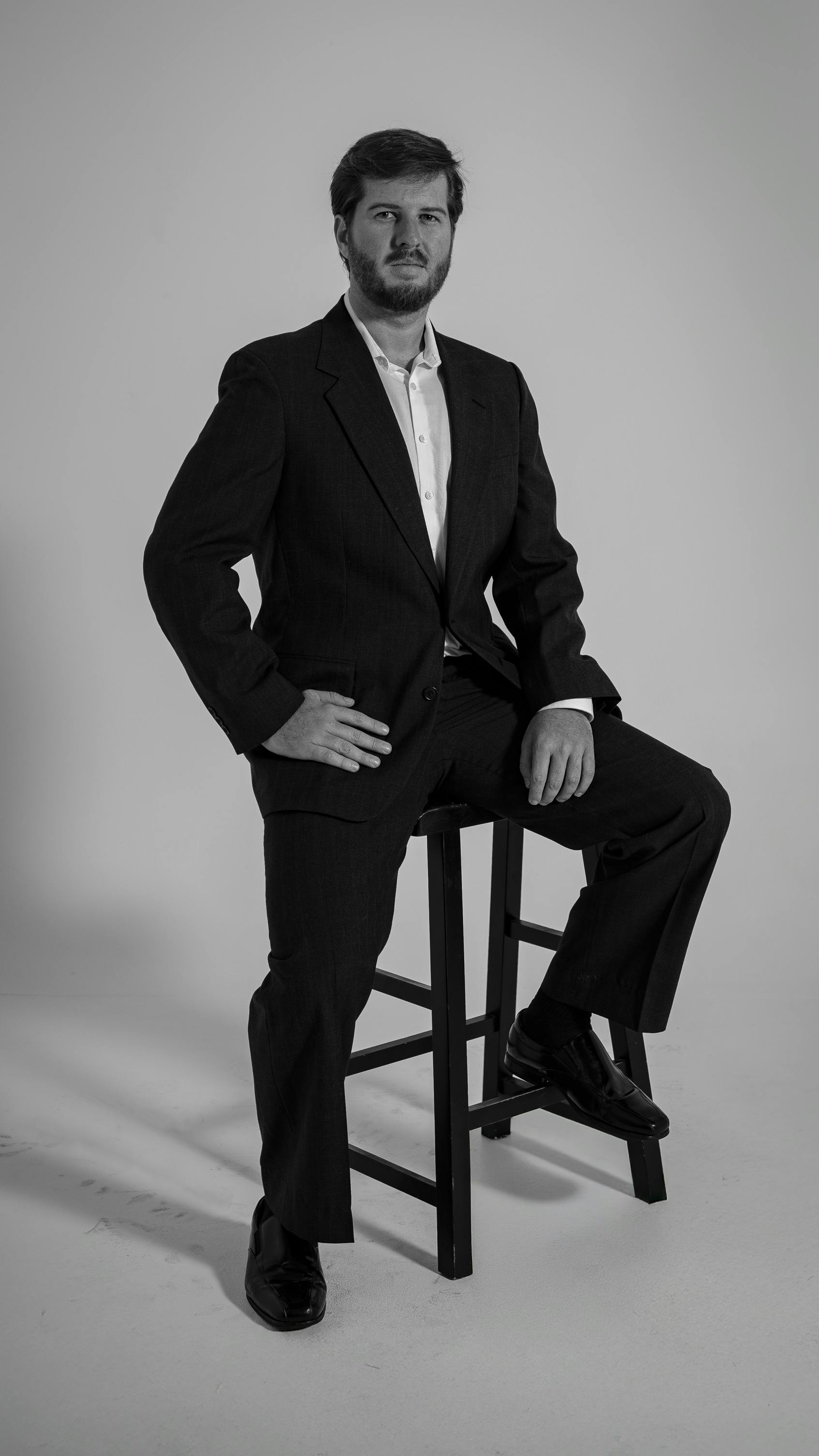 Gratis Professionelt portræt af en mand i et jakkesæt, skudt i sort og hvid, siddende på en skammel. Lagerfoto