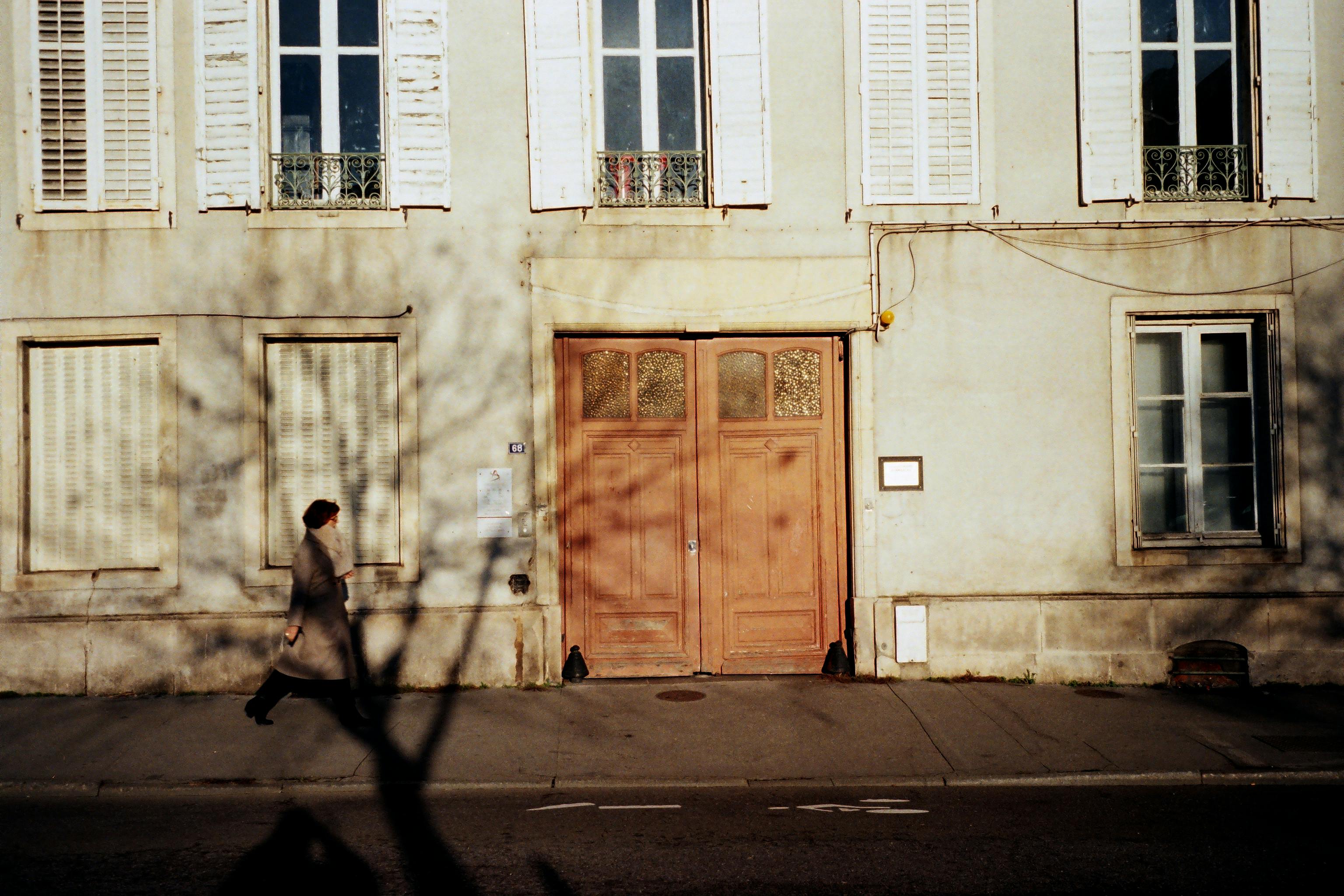A person walks past a historic building facade in Nancy, France, with shadows cast on the wall.