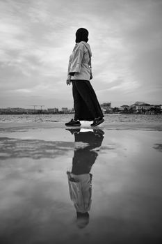A woman walks near a reflective puddle, creating a moody silhouette.
