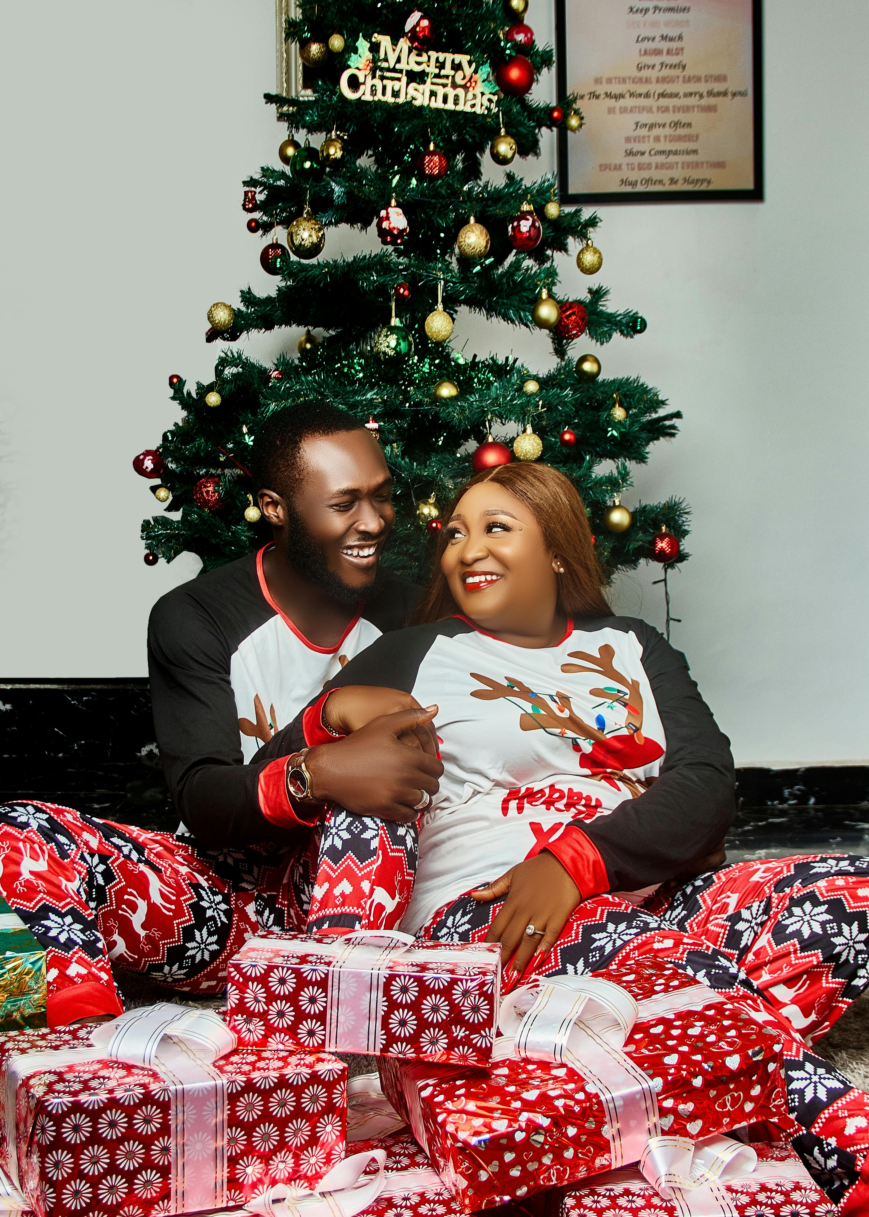 Smiling couple in matching pajamas by Christmas tree surrounded by gifts.