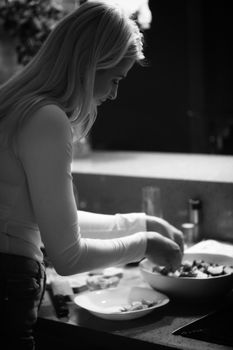 A woman preparing a meal in a modern kitchen, captured in black and white.