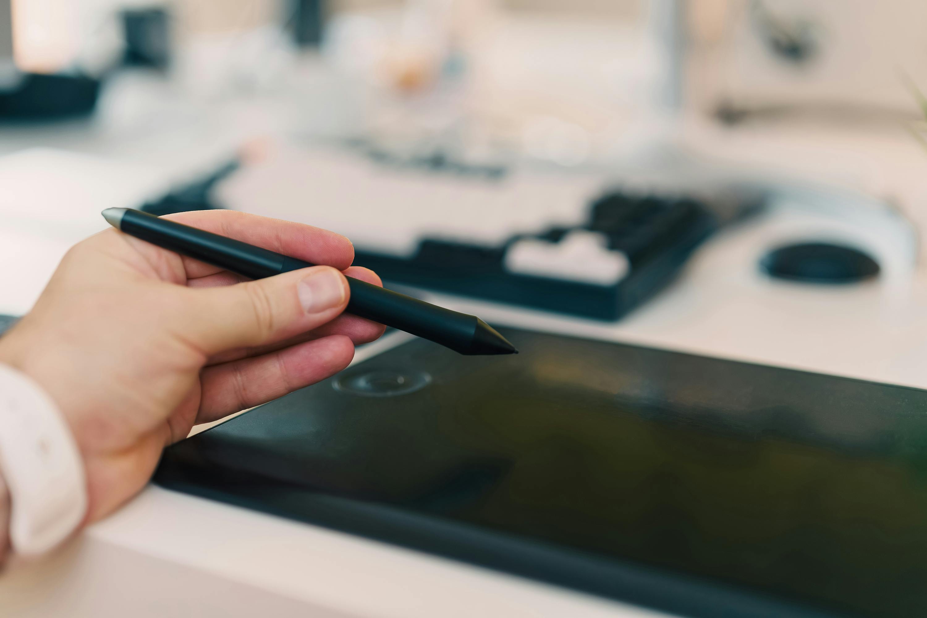 Close-up of a hand using a stylus on a digital tablet in an office setting.