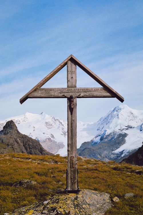 Free A striking wooden cross stands before a breathtaking mountain vista with snow-capped peaks. Stock Photo