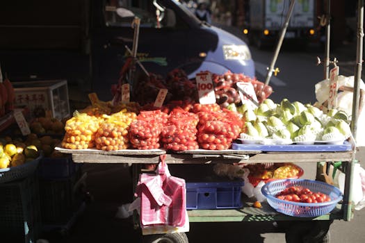 Colorful display of fruits in an outdoor market, featuring tomatoes, guavas, and oranges.
