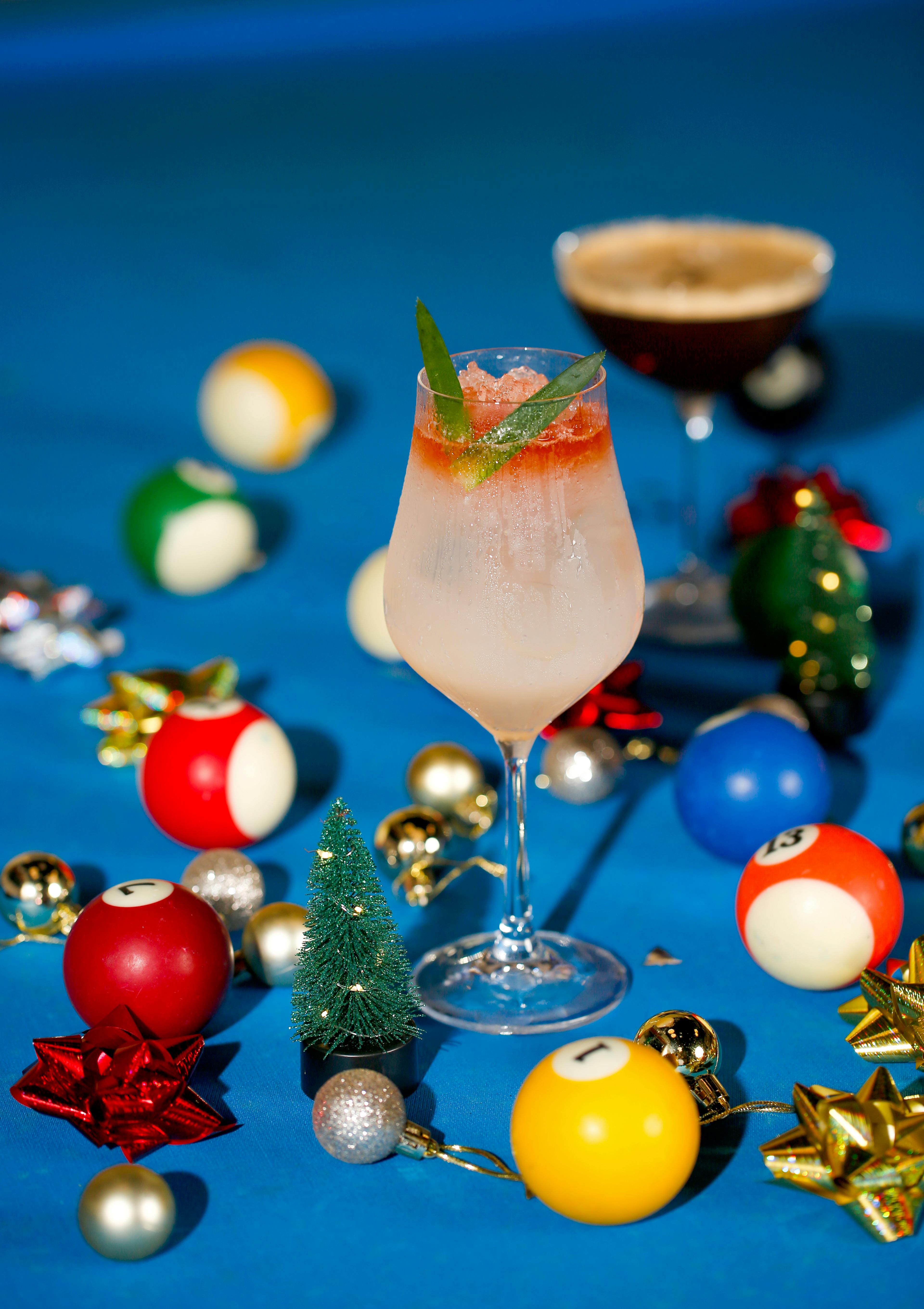 A festive cocktail surrounded by pool balls and holiday decorations on a blue surface.
