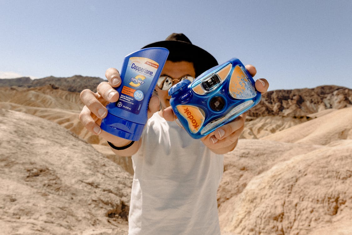 Man holding up sunscreen and a disposable camera