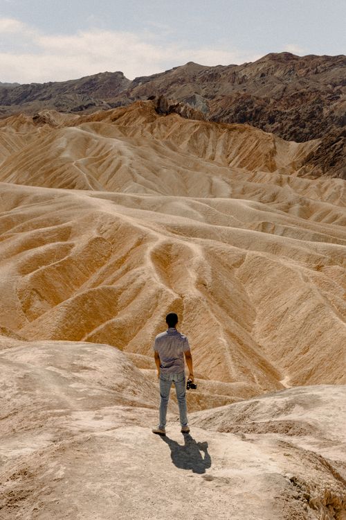 Free A lone man stands in a vast, arid desert landscape, exploring and contemplating the rugged terrain. Stock Photo