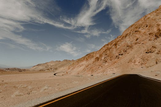 Vast desert road with dramatic sky and rocky mountain landscape.