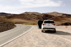 White SUV parked along a winding desert road under clear skies, showcasing adventure and travel.