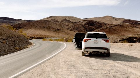 White SUV parked along a winding desert road under clear skies, showcasing adventure and travel.