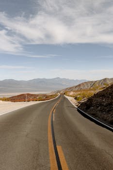 Long stretch of desert highway leading into distant mountains under a clear sky.
