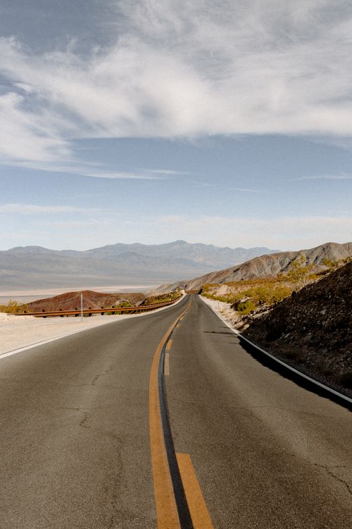 Free Long stretch of desert highway leading into distant mountains under a clear sky. Stock Photo