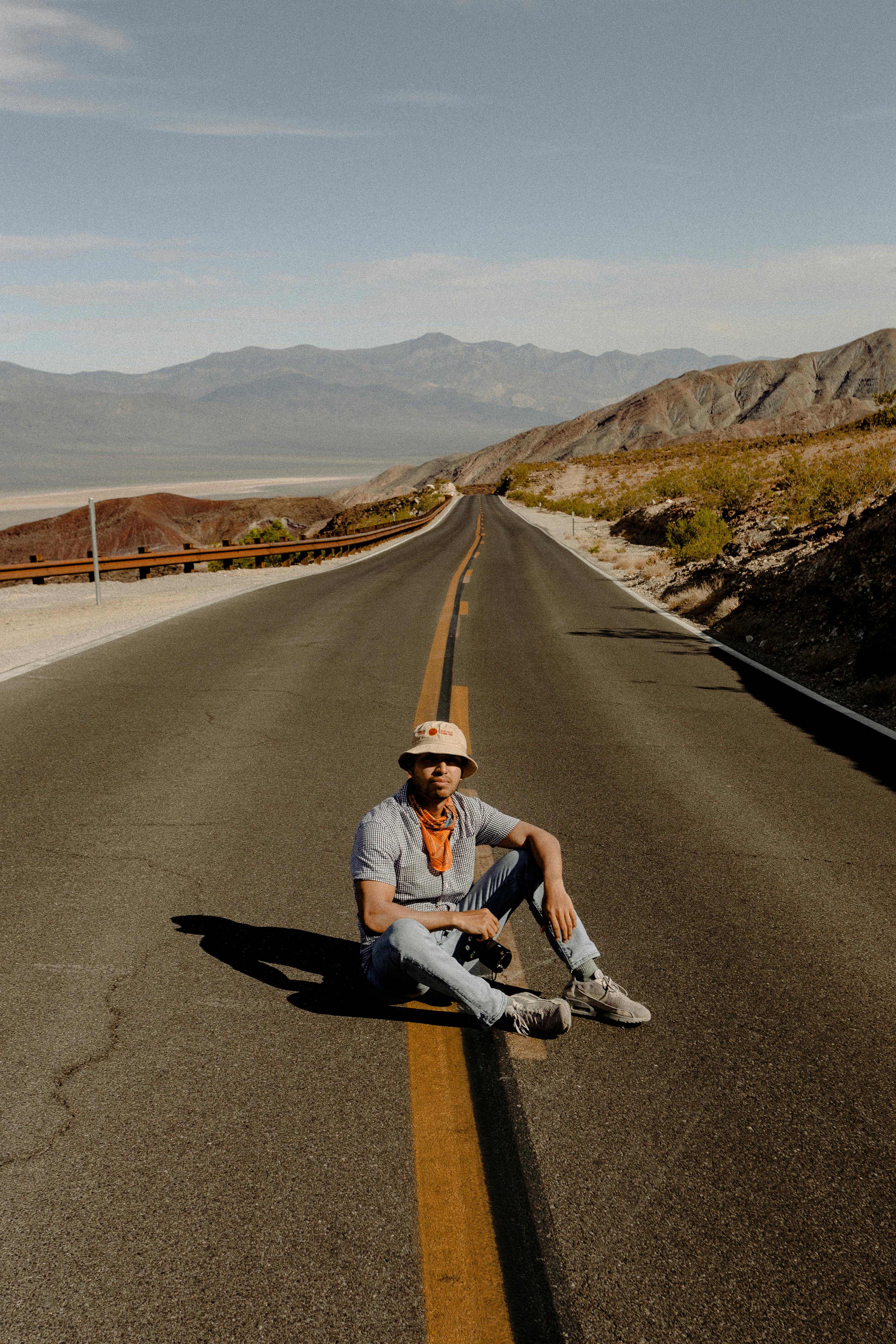 Casually dressed man sits on a deserted mountain highway on a sunny day.