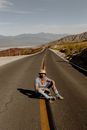 在荒无人烟的山区高速公路上，一名衣着随意的男子坐在阳光下