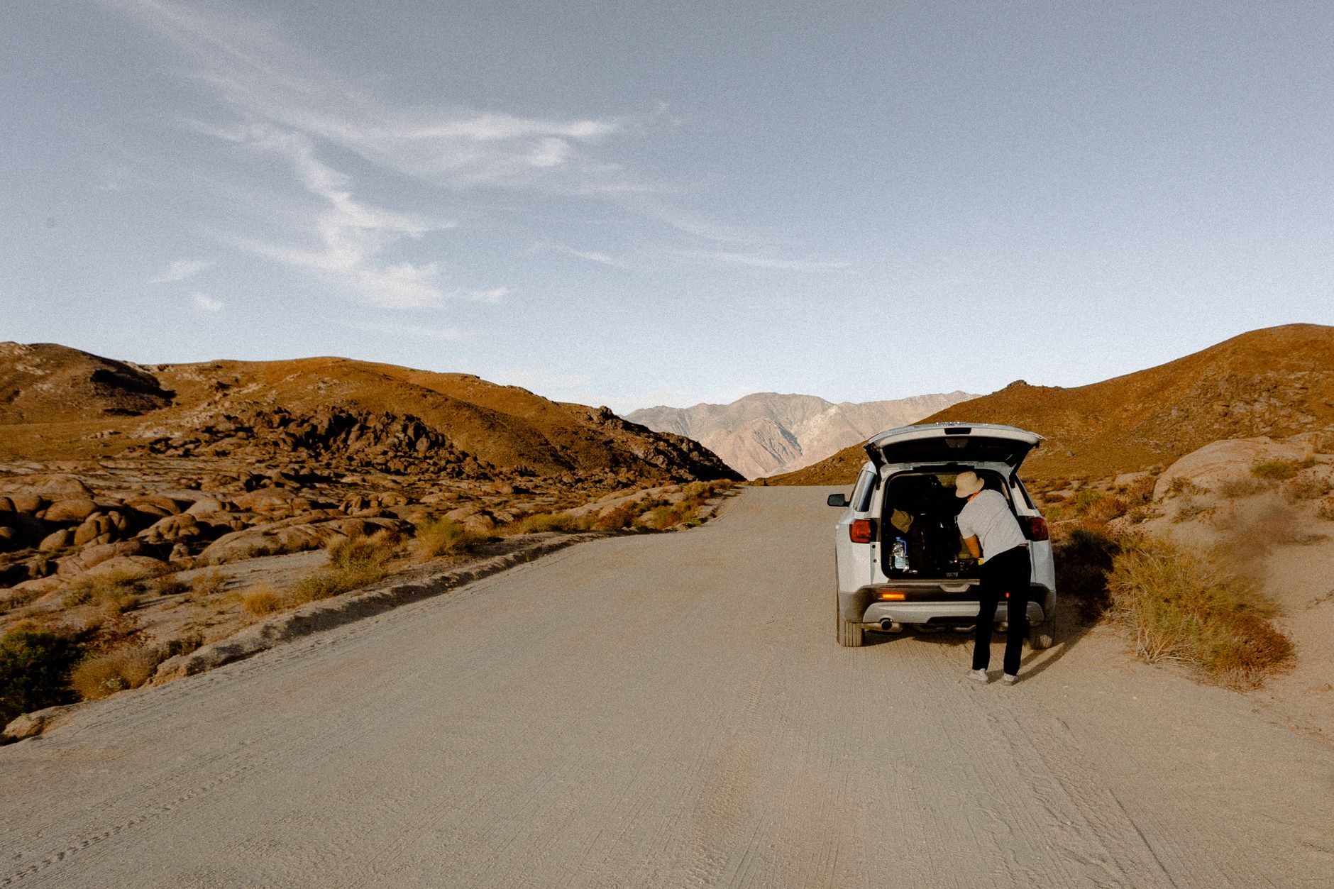 Person organizing gear in SUV on isolated desert road, perfect for travel enthusiasts.