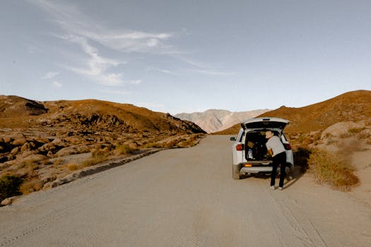 Person organizing gear in SUV on isolated desert road, perfect for travel enthusiasts.