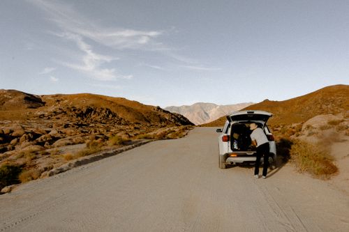 Free Person organizing gear in SUV on isolated desert road, perfect for travel enthusiasts. Stock Photo