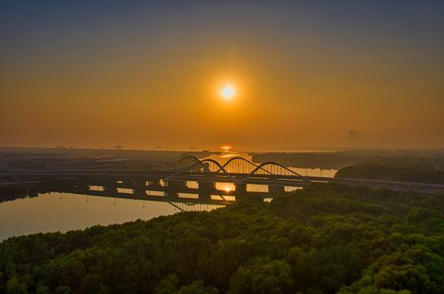 Free Stunning sunrise view of a bridge in Jakarta, Indonesia, with a golden sky reflecting on the water. Stock Photo