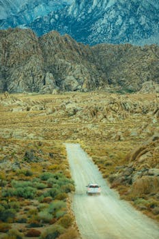 A vehicle driving on a dirt road through a rocky mountain landscape, showcasing adventure and travel.
