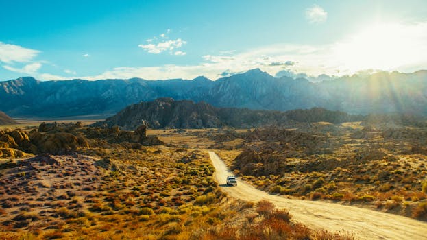 Car driving on a dirt road through a vast mountain landscape at sunset.