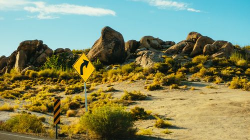 Free A road sign in a desert landscape with large boulders and shrubs under a clear blue sky. Stock Photo