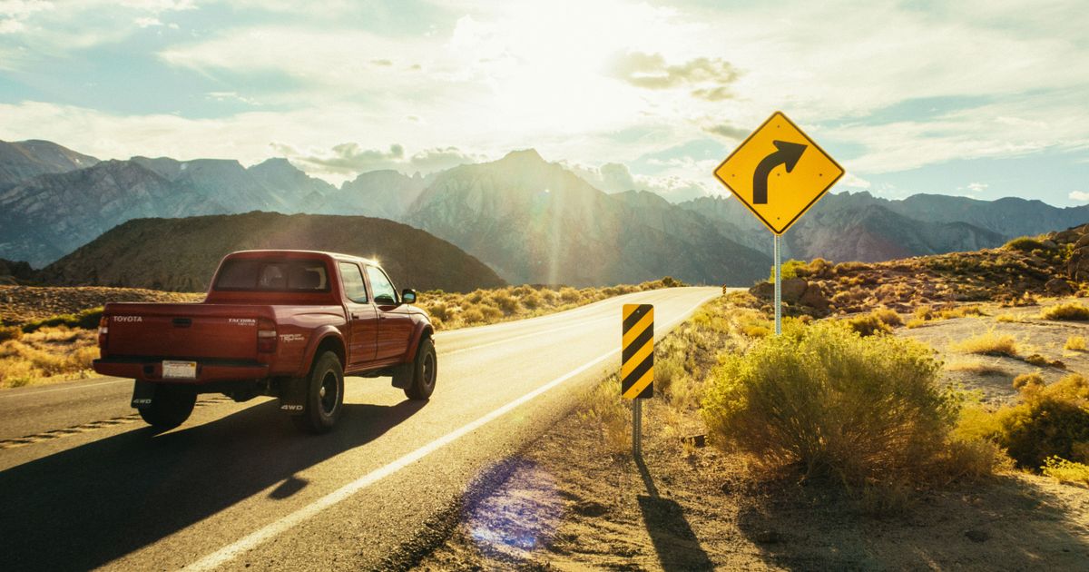 A red pickup truck driving on a sunlit highway.