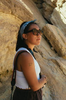 一名戴着太阳镜和头巾的女子，在阳光明媚的岩石景观中用相机捕捉瞬间