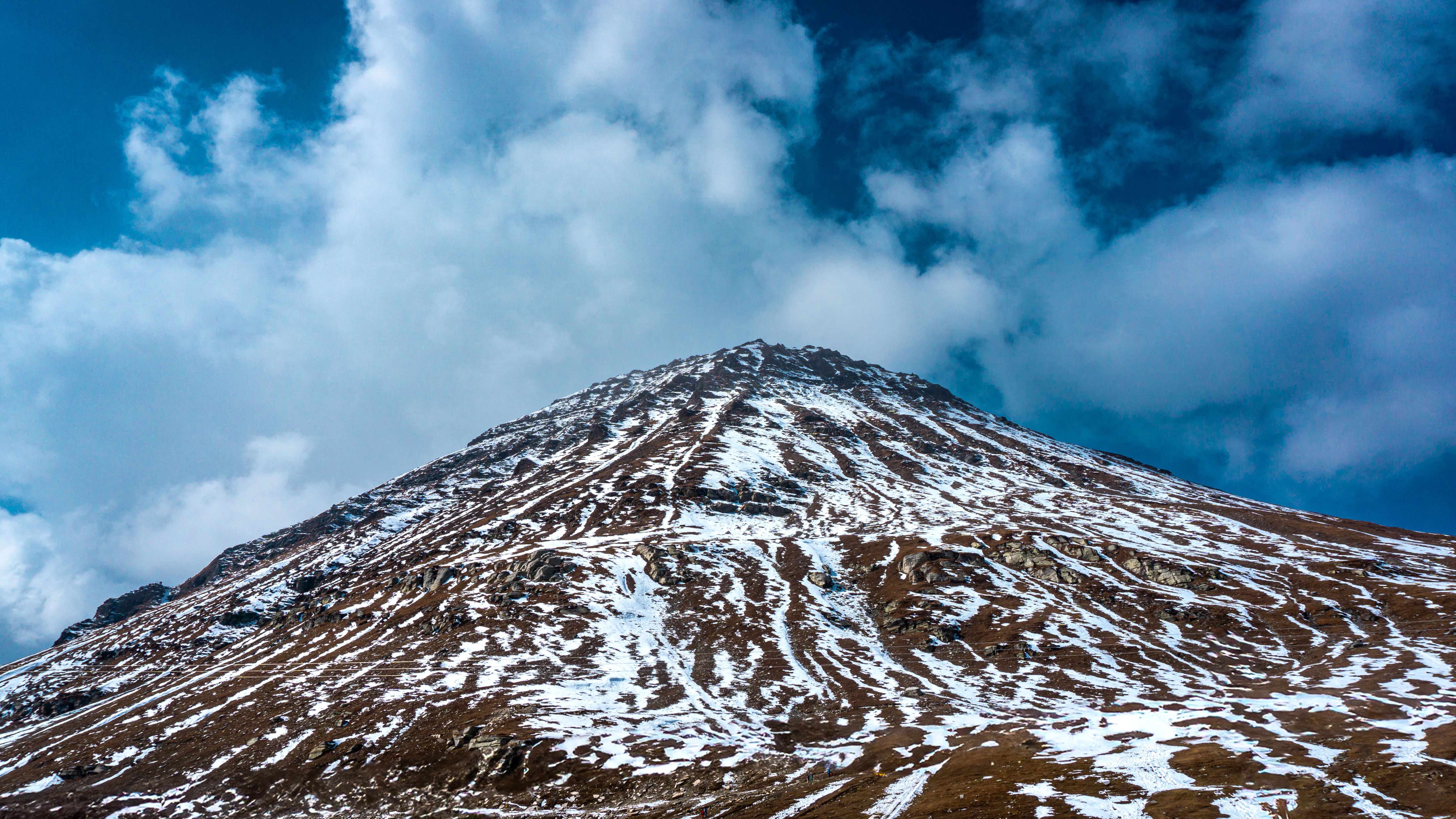 A stunning view of a snow-covered mountain peak under a cloudy blue sky, showcasing nature's beauty.