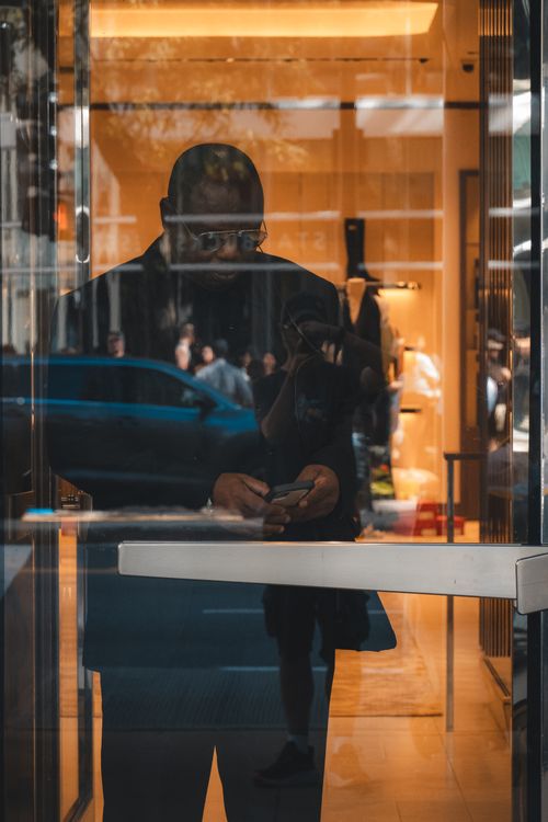 Free Reflection of a person using a smartphone through a glass door with urban background. Stock Photo