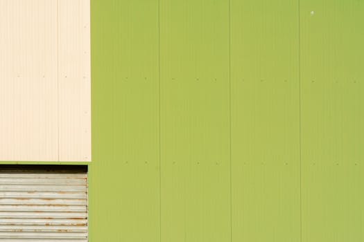 Industrial green facade with abstract forms and garage door detail.