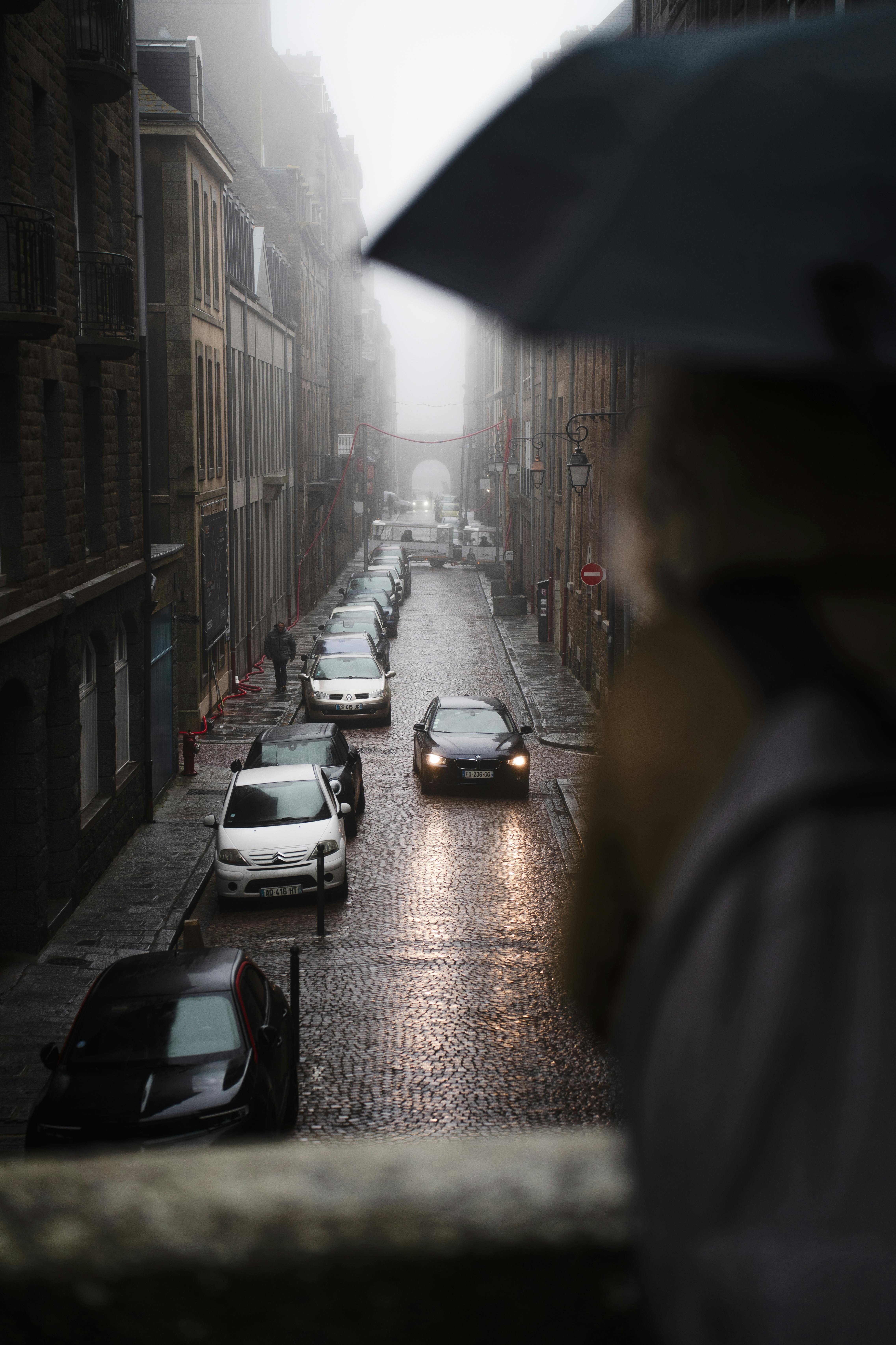 Moody rainy day in Saint-Malo's cobblestone street view with cars and an umbrella.