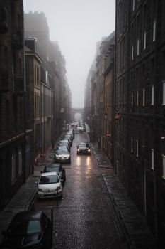Foggy street view of Saint-Malo, France, with cars parked along cobblestone roads.