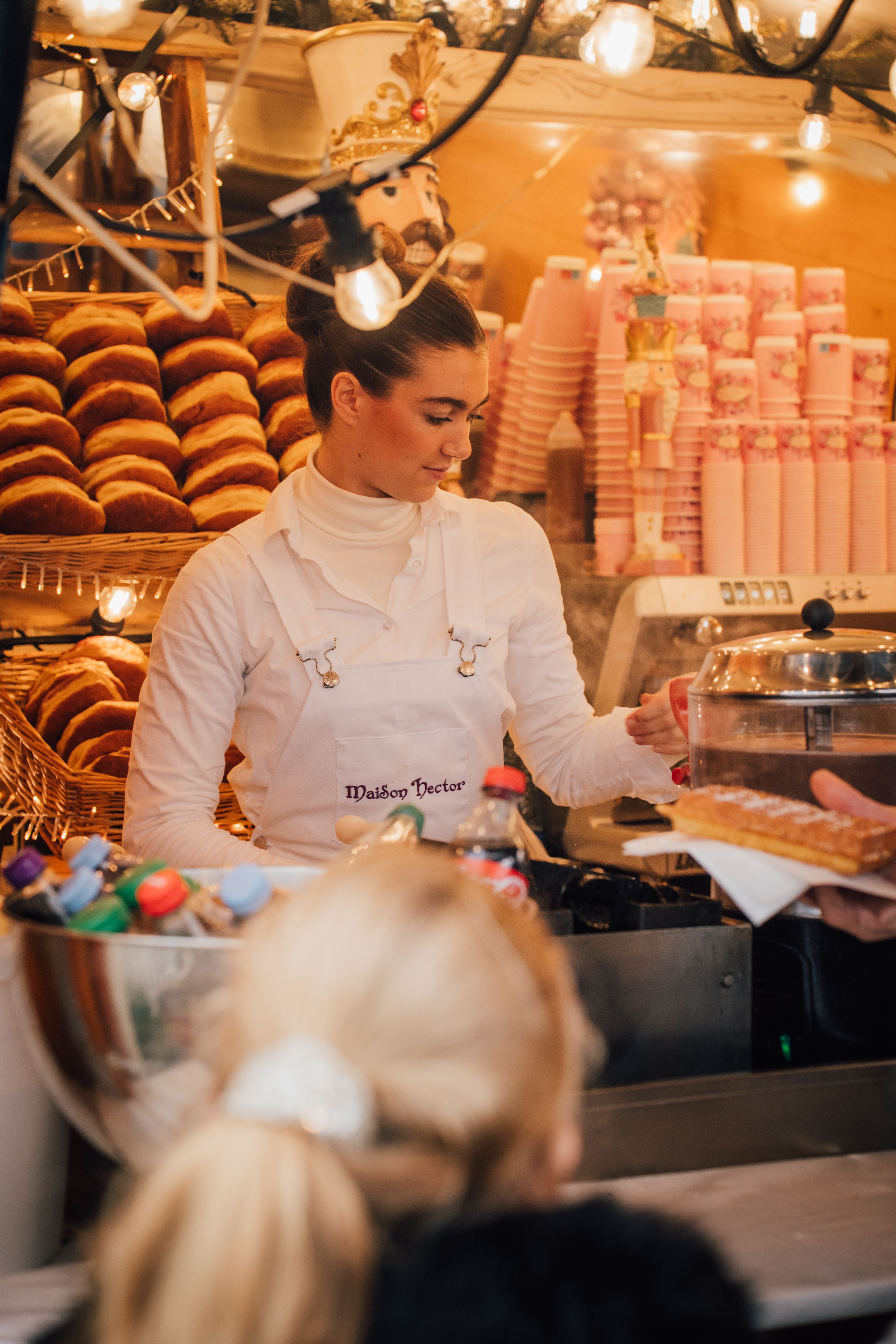 Woman serving pastries at a vibrant market stall in Saint-Malo, France.