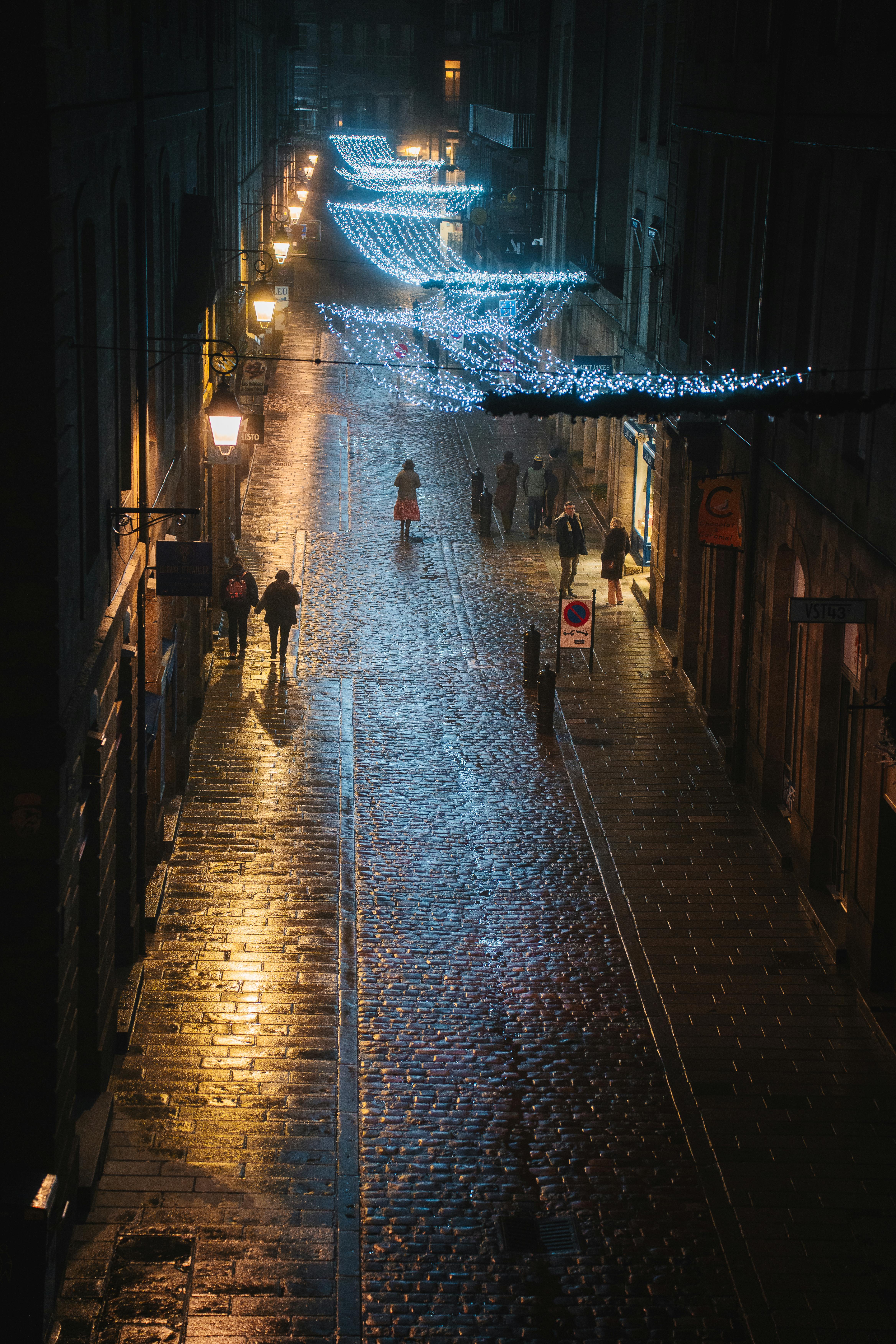 Street view of Saint-Malo, France, with festive lights and wet cobblestones at night.