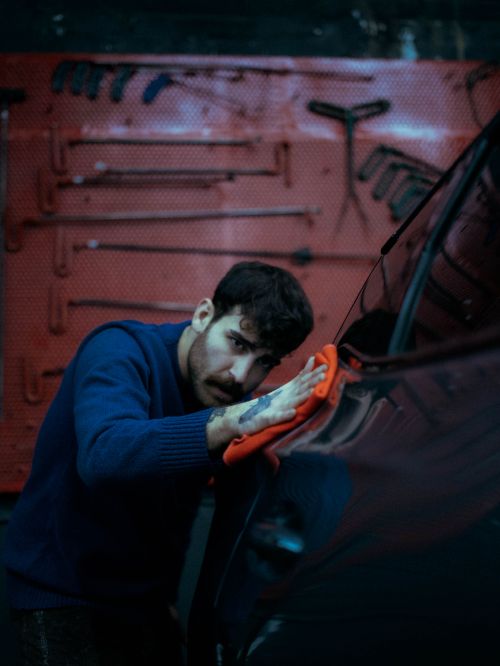Free A young man polishing a car in a garage, showcasing attention to detail and care. Stock Photo