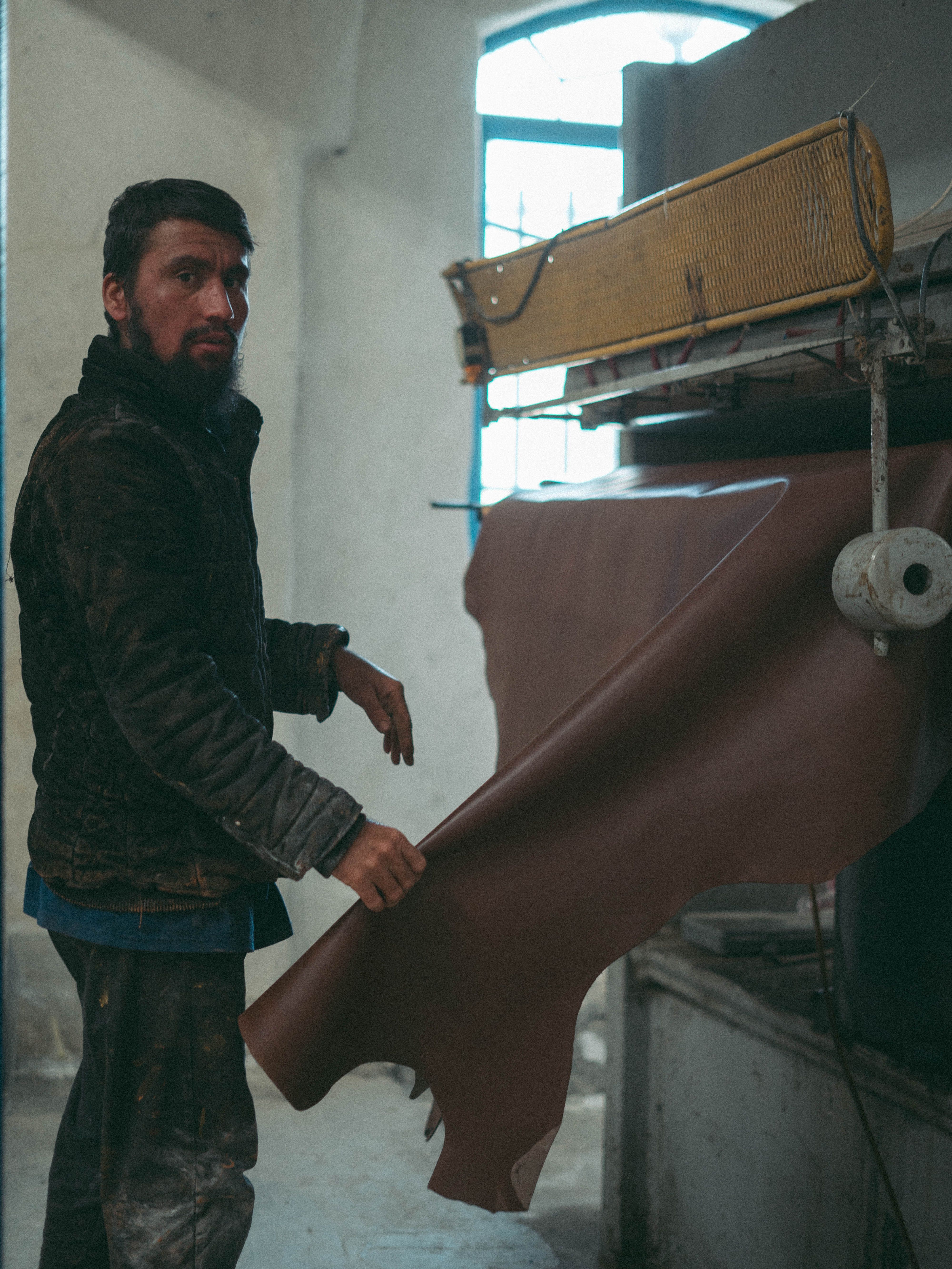 A craftsman handles a large leather piece in a workshop, showcasing traditional workmanship.