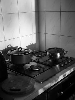 Black and white photo of a stove with cooking pots, creating a warm, homely feel.