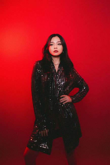 Dramatic portrait of a woman in a sequined outfit against a red backdrop.