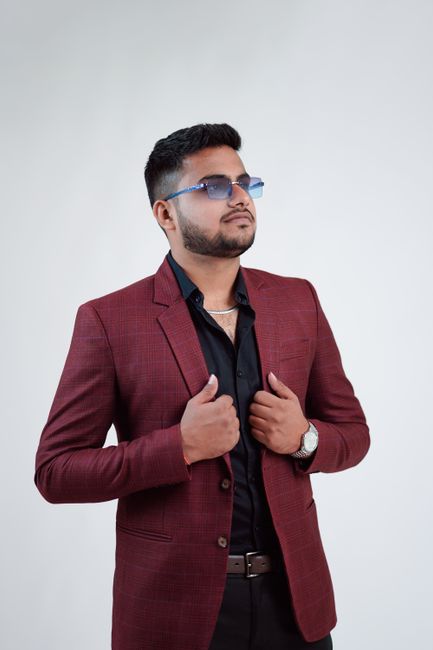 A young man poses confidently in a stylish red blazer and sunglasses against a neutral background.