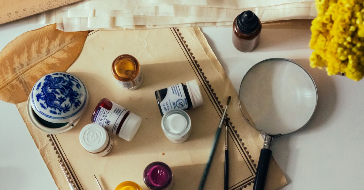 Artistic tools including paints and magnifying glass flat lay.