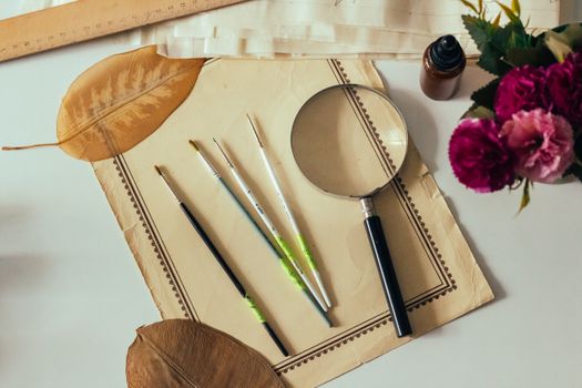 Aesthetic flat lay featuring paintbrushes, magnifying glass, and dried leaves.