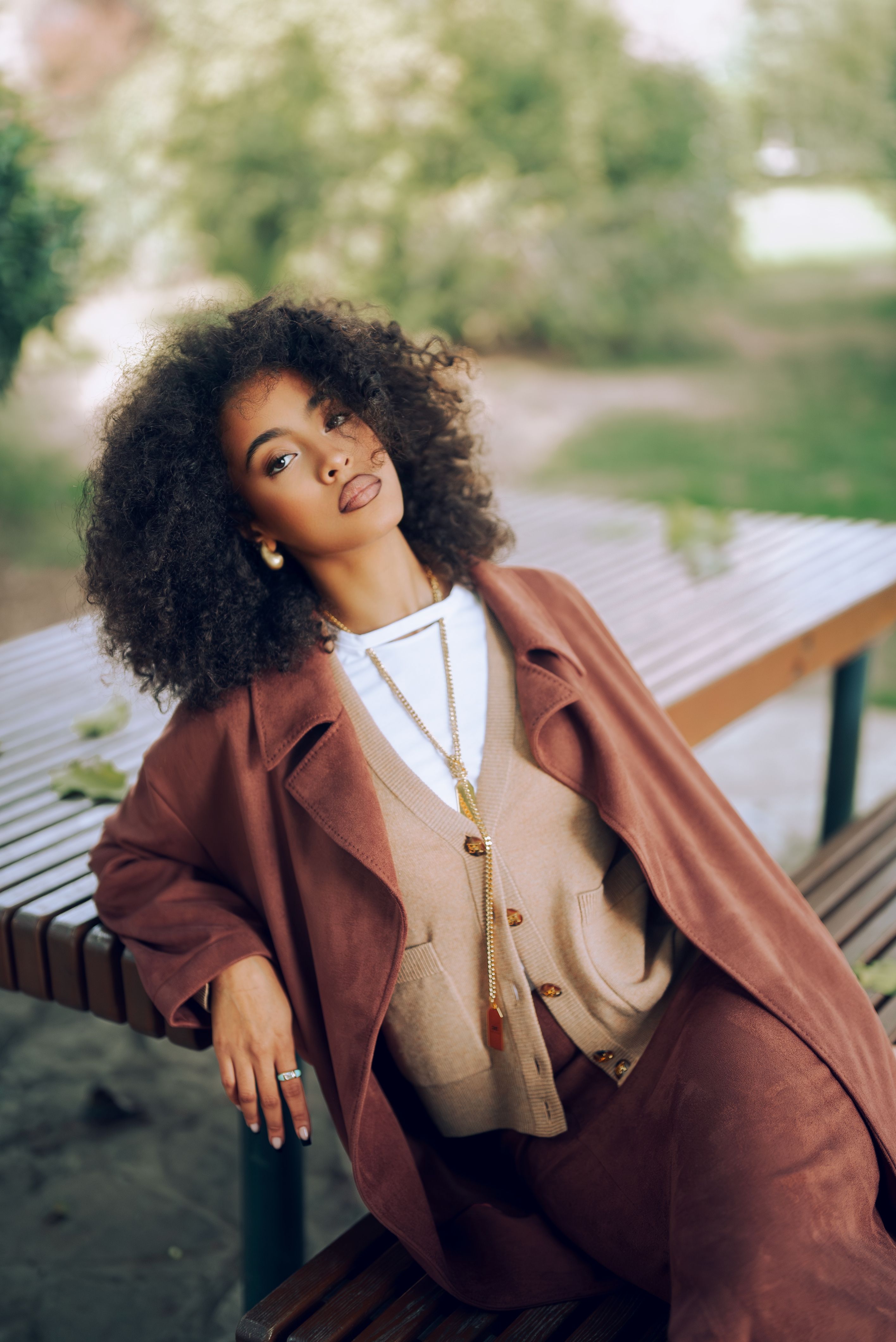 Casual portrait of a stylish woman in autumn attire relaxing on a bench in a park.