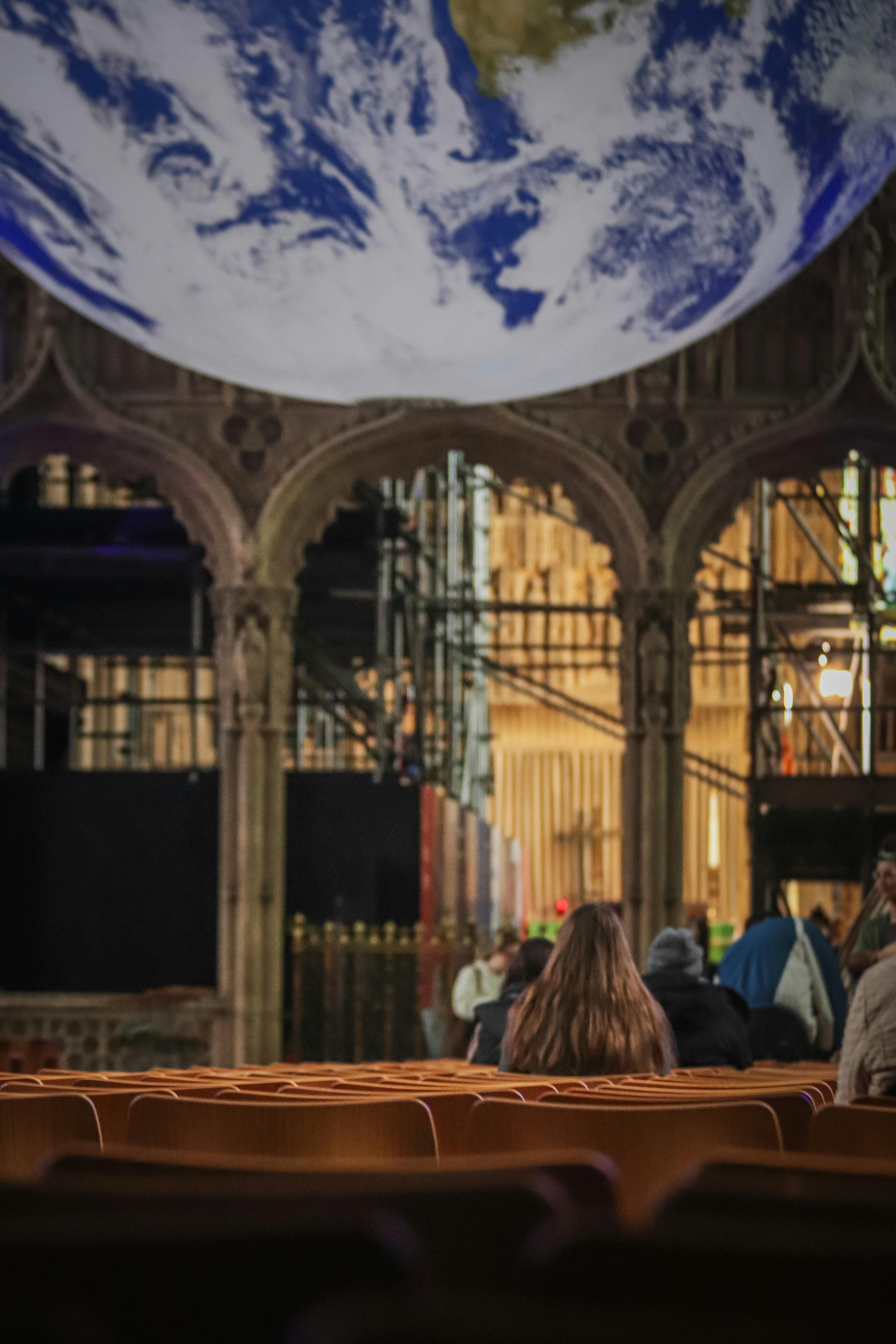grátis Cena de sala de concertos com globo terrestre e plateia, transmitindo um tema global em ambientes fechados. Foto profissional
